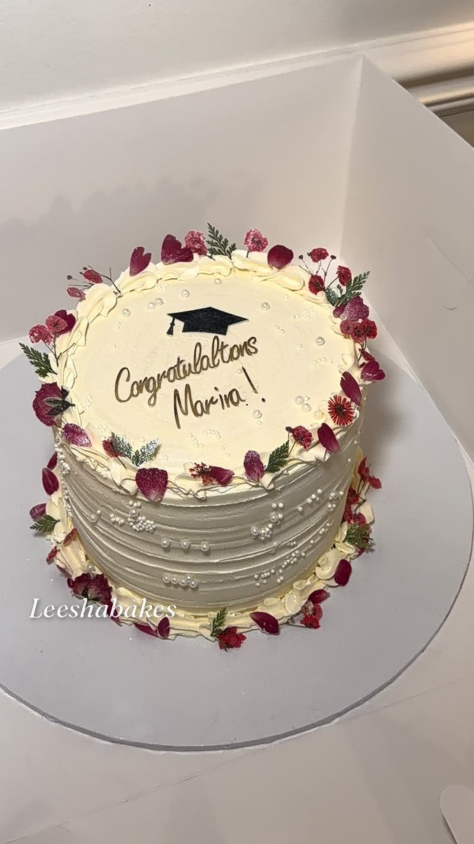 Cream cake with pressed flowers, graduation cap and 'Congratulations Marina' message