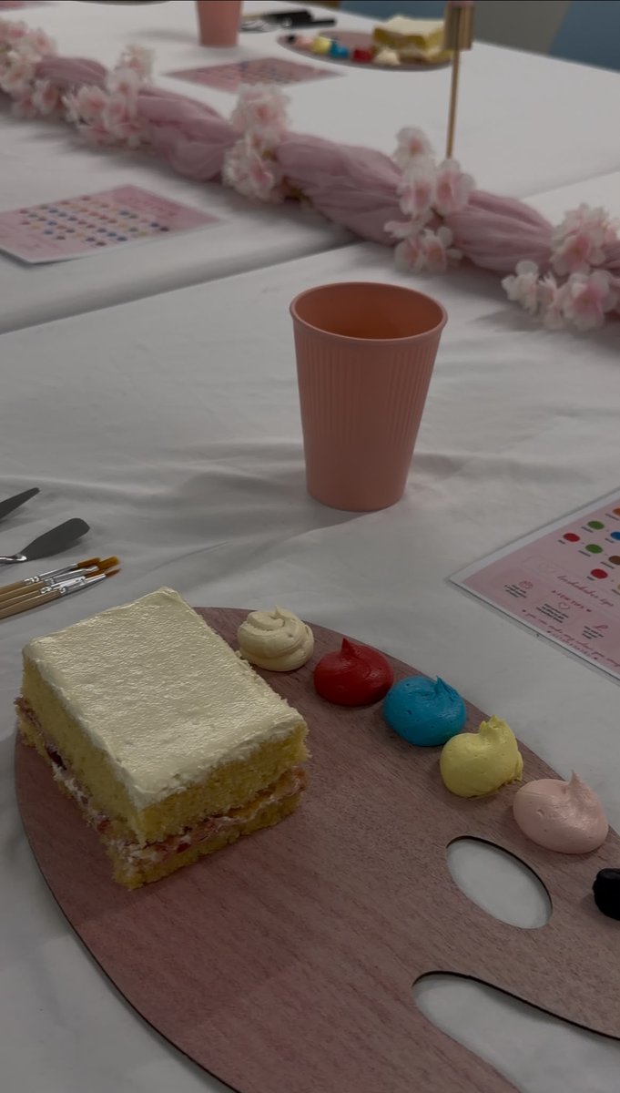 Square sponge cake on a palette board beside red, blue, yellow and pink buttercream paints