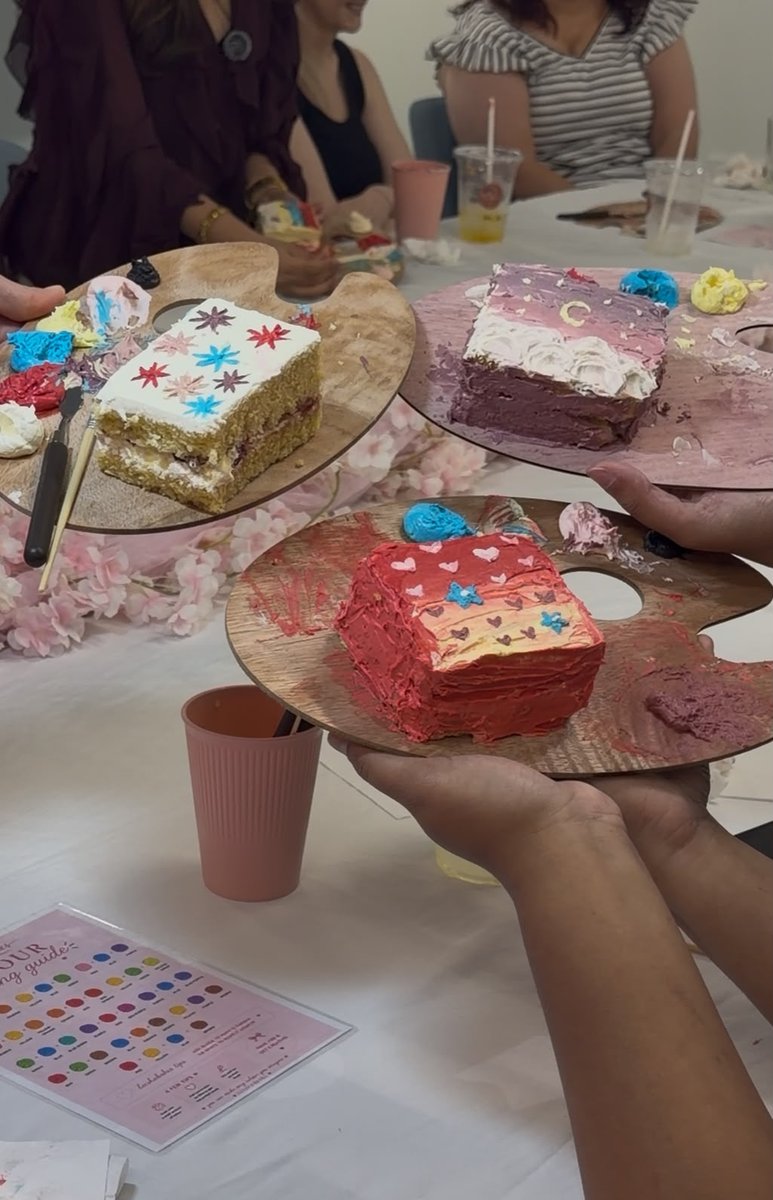 Three finished hand-painted cakes held up on palette boards at the cake painting experience
